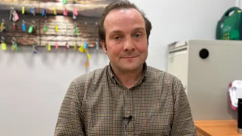 Estate agent James Spring is sitting in an office with a filing cabinet behind him