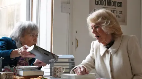 PA Media The Queen is looking at a book that is being shown to her.