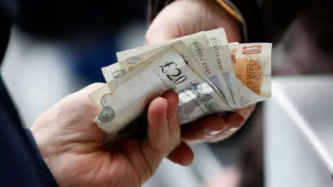 A close-up of a person handing over a wad of cash to another person. 