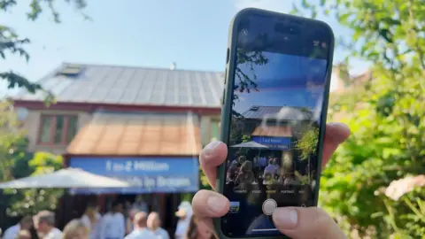 A person holds up a mobile phone to take a picture of the UK's first ever house to be build with a solar roof 30 years ago