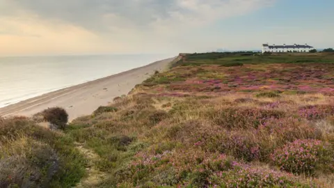 Justine Minns/National Trust Cliffs covered in heather and beaches at Dunwich, with Coastguard cottages in the background