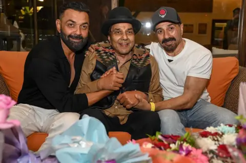 AFP via Getty Images Bollywood actor Dharmendra (C) along with his sons Sunny Deol (R) and Bobby Deol (L) pose for a photo on the occasion of his 89th birthday at his residence in Mumbai on December 8, 2024. (Photo by Sujit JAISWAL / AFP) (Photo by SUJIT JAISWAL/AFP via Getty Images)