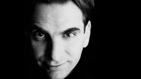 A black and white close-up image of Langlois. He has black hair and thick black eyebrows, and is smiling slightly at the camera.