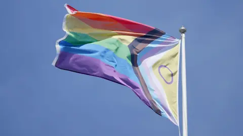 A pride flag on a flagpole blowing in the wind.