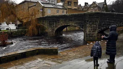 Getty Images A mum and child stand next to a river in the rain. A stone bridge, with some properties behind it can be seen.