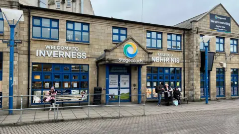 A straight on view of the entrance to the Inverness Bus station building. A sign on the the building says "welcome to Inverness", "Failte Gu Inbhir Nis" and there is also a Stagecoach sign above the door.