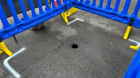 George Carden / BBC The sinkhole surrounded by plastic fencing. It is the size of a tennis ball on the surface but about six foot wide underneath