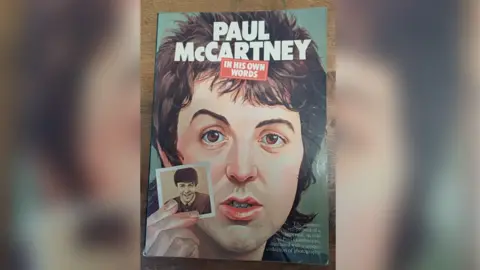 Front cover of the Paul McCartney book. It has a cartoon image of Paul McCartney holding a photo inset of himself.