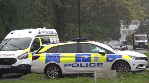 A police car and van are parked in the rain in a residential area in Crawley