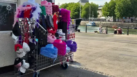 A street vendors stand with colourful hats and trinkets set up by Bristol Harbourside.