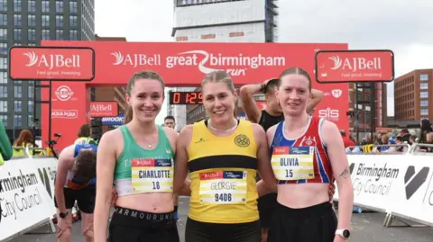 Great Birmingham Run Charlotte Bush, Georgie Campbell and Olivia Bailey are standing together at the finish line for a photograph. They are wearing their running gear.