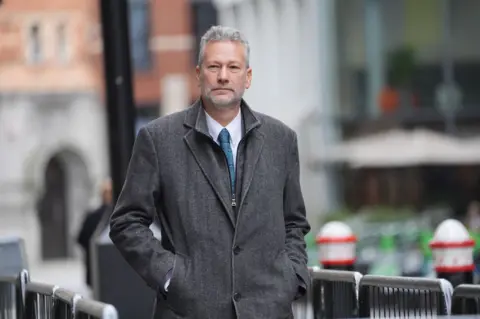 PA Media A man with white hair, wearing a grey jacket and green tie