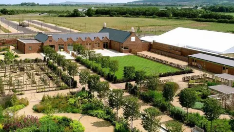 Redcar and Cleveland Council An aerial image of Kirkleatham Walled Garden, with various sections of gardens with different plants and features. There are several red-brick buildings all around the central garden section.