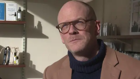 Brendan Murdock, wearing glasses and with a shaven head, looks at the camera