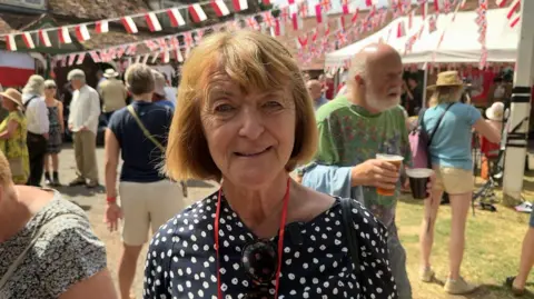 Stanislawa with brown hair and a dark patterned top standing with a crowd of people and bunting behind her.