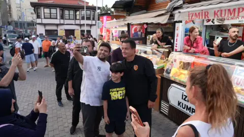 Acun Ilicali poses for a photograph with members of the public at a street food market in Istanbul.