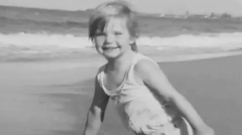 Cheryl Grimmer smiling at the camera near the sea as a young girl