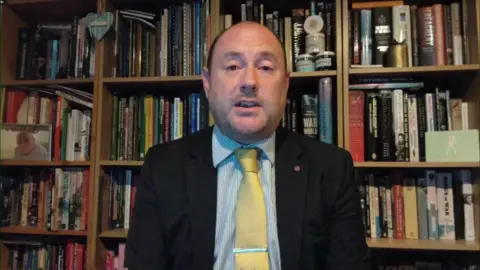 Matthew Searle, the chief executive of LBT Global, sits in front of a bookshelf being interviewed for BBC News