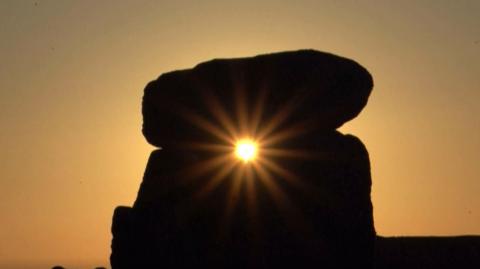 The sun visible at sunset through one of the structures at stonehenge