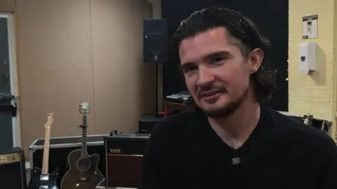 James in his practice room, guitars and amps behind him.