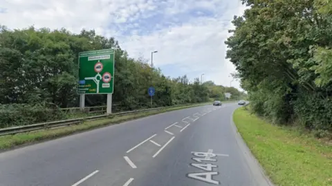 A screengrab from Google Maps of the A419, with trees on either side and a big green road sign