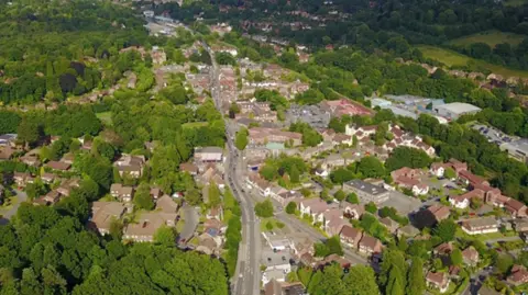 An aerial view of a town in Waverley. A number of houses can be seen either side of a road running directly through the town. There are also a number of green trees in the image.