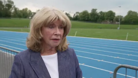 Denise Jeffrey, who has blonde hair and blue eyes. She is wearing a blue blazer with a white t-shirt.