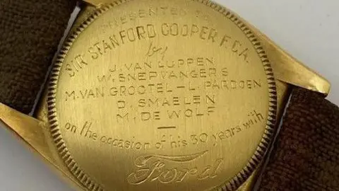 Kinghams Auctioneers The gold back case of a Rolex watch, which has woven brown fabric straps. The back is inscribed with the words "Presented to Sir Stanford Cooper F.C.A. by J. Van Luppen, W. Snepwangers, M. Van Grootel - L Pardoen, D. Smaelen, M. De Wolf, on the occasion of his 30 years with Ford.