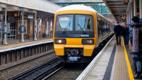 A white Southeastern train with a yellow and black front going to London Victoria arriving at Beckenham Junction Station in North West Kent (Greater London). Passengers on the platform are standing well back to avoid accident.