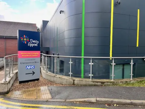 The exterior of the Molecular Imaging Research Centre at Castle Hill Hospital. The building is covered in dark grey cladding and has colourful stripes as part of the design.