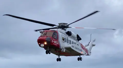 A red and white coastguard helicopter photographed against a dark grey sky