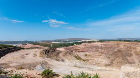 A wide view of Hermerdon mine in Devon. The land is light brown with dark patches and is deep. 