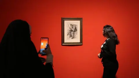 Fatemeh Bahrami/Getty Images A woman looks at a Van Gogh artwork on display on a red wall