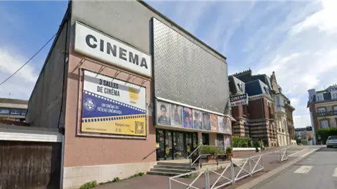 Google A modern, brick and slate cinema building in a small street. A sign says 3 Salles de Cinema (Three Cinema Screens).