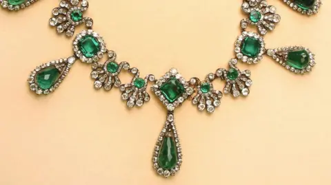 Gamma-Rapho via Getty Images An ornate emerald necklace on a yellow background
