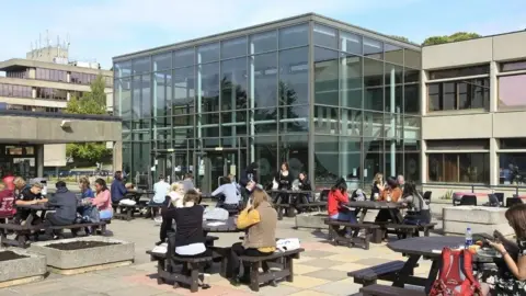 Getty Images Students sitting on picnic tables on a patio outside UEA building made of glass and concrete