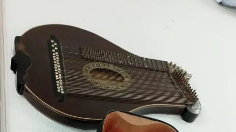 The harp is a dark brown colour with a decorative opening in the body of the instrument. There is a neck at the top of the instrument like there would be on a guitar. There are tens of strings beneath this. 