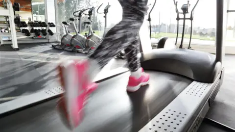 A person in leggings and pink trainers running on a treadmill. The image is blurred in the foreground.