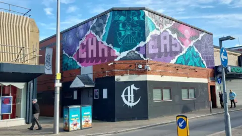 Chasers night club from the outside. The building is black with a colourful graffiti on the top of the building.