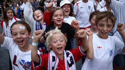 Reuters Young England fans, boys and girls, in red and white colours, cheering with their arms in the air.