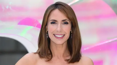 Close up of Jones who has shoulder-length brown hair and is smiling at the camera.