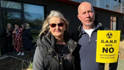 James Turner/LDRS Protesters outside council offices in Horncastle. A man with short hair is holding a placard which reads: Gayton says no - Gayton against nuclear dump. A woman wearing a black coat and sunglasses stands next to him.