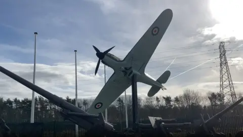 BBC/Marley Styles A WW2 fighter plane and tank display at Eden Camp Museum. The fighter plane has grey wings and a dark propeller. 