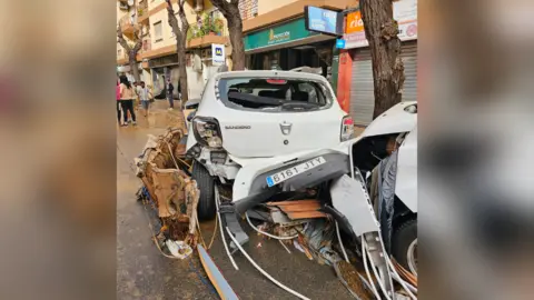 Julio Albir A white car is wrecked after flooding in Valencia. The back of the car is crumpled and the back window is missing. 