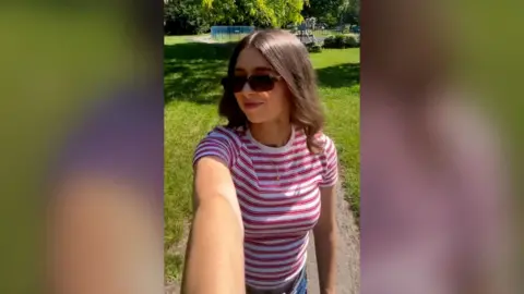 Selfie view of a woman outside wearing sunglasses and stripy top, in a park