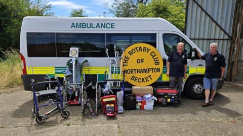 Two men stand by an ambulance with wheelchairs and crutches in the foreground