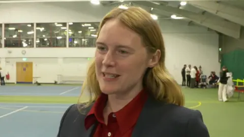 Labour MP for South East Cornwall Anna Gelderd standing inside a sports hall. She is wearing a shirt and blazer.