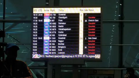 Reuters A camera person stands next to a screen displaying flights cancelled by IndiGo Airlines at the Indira Gandhi International Airport in Delhi, India, December 5, 2025. REUTERS/Bhawika Chhabra