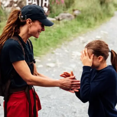 Instagram/princeandprincessofwales Kate looks at Charlotte who covers her face while a boy plays with a dog in the background 
