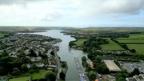 A picture of Kingsbridge taken from above, with an estuary in the centre. There is a number of properties either side of the water, plus green fields in the distance.